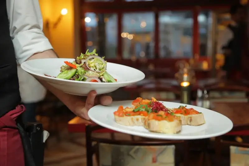 Un camarero experto demuestra cómo servir una mesa, presentando un plato de ensalada fresca y bruschettas.